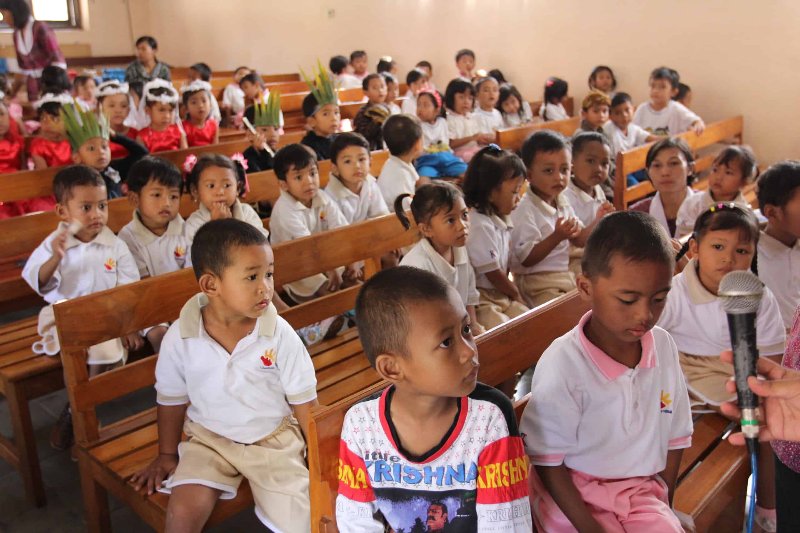 Anak-anak sekolah minggu duduk di bangku gereja mengikuti acara